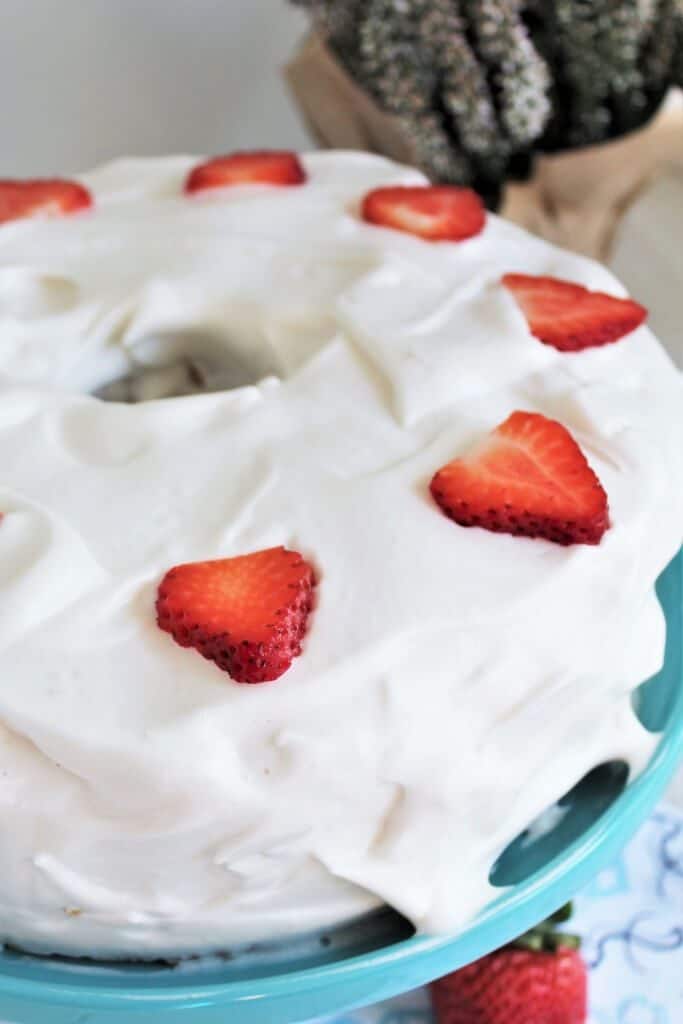 A finished vegan angel food cake topped with whipped cream and strawberries. 