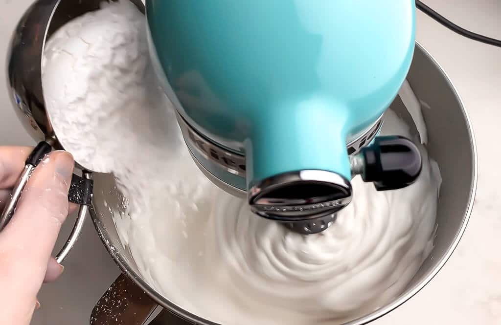 Powdered sugar being added to aquafaba whipped cream while blending it.