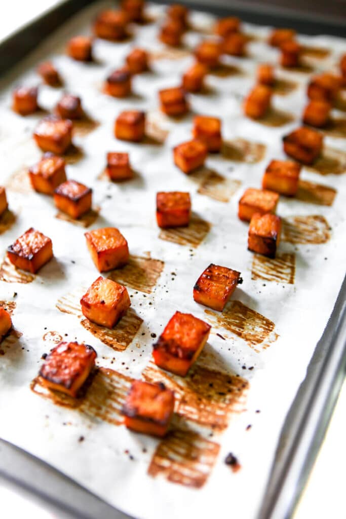 Cubes of tofu on a baking sheet that has been lined with parchment paper.