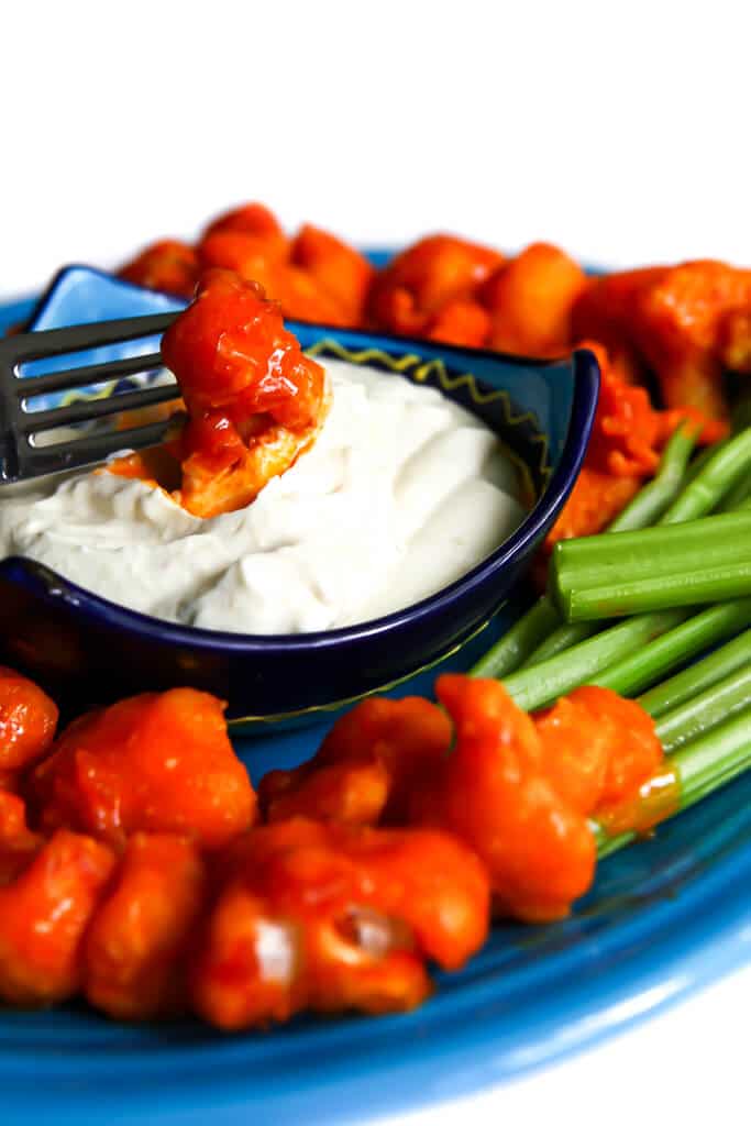 Buffalo cauliflower being dipped into vegan blue cheese dressing.