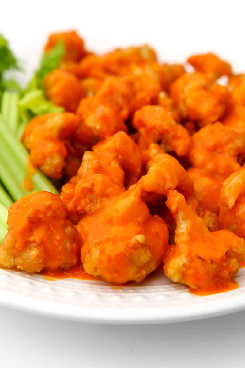  A white plate filled with buffalo cauliflower nuggets with celery on the side.