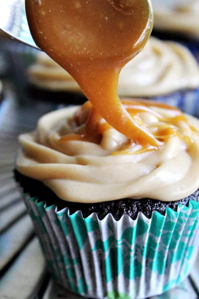 A chocolate cupcake in a blue wrapper with vegan caramel frosting and salted caramel sauce being drizzled over top of it.
