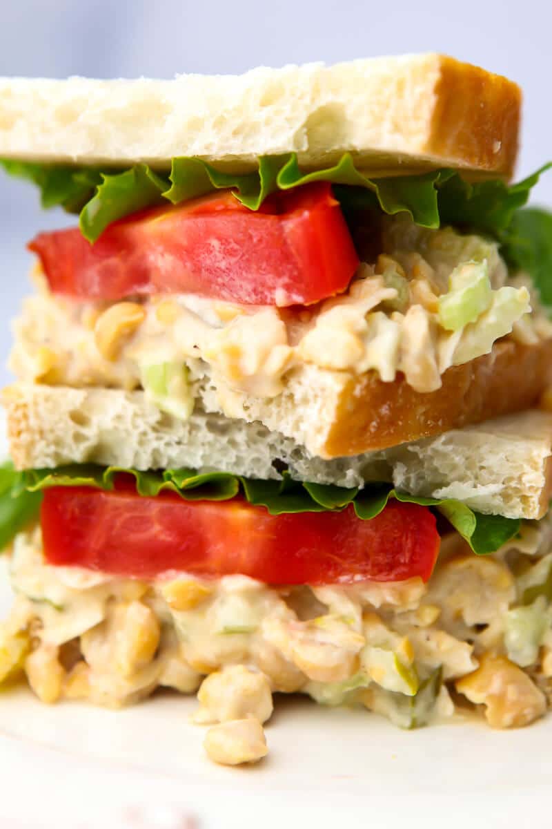 A close up of a vegan chickpea salad sandwich with lettuce and tomato slices on it.
