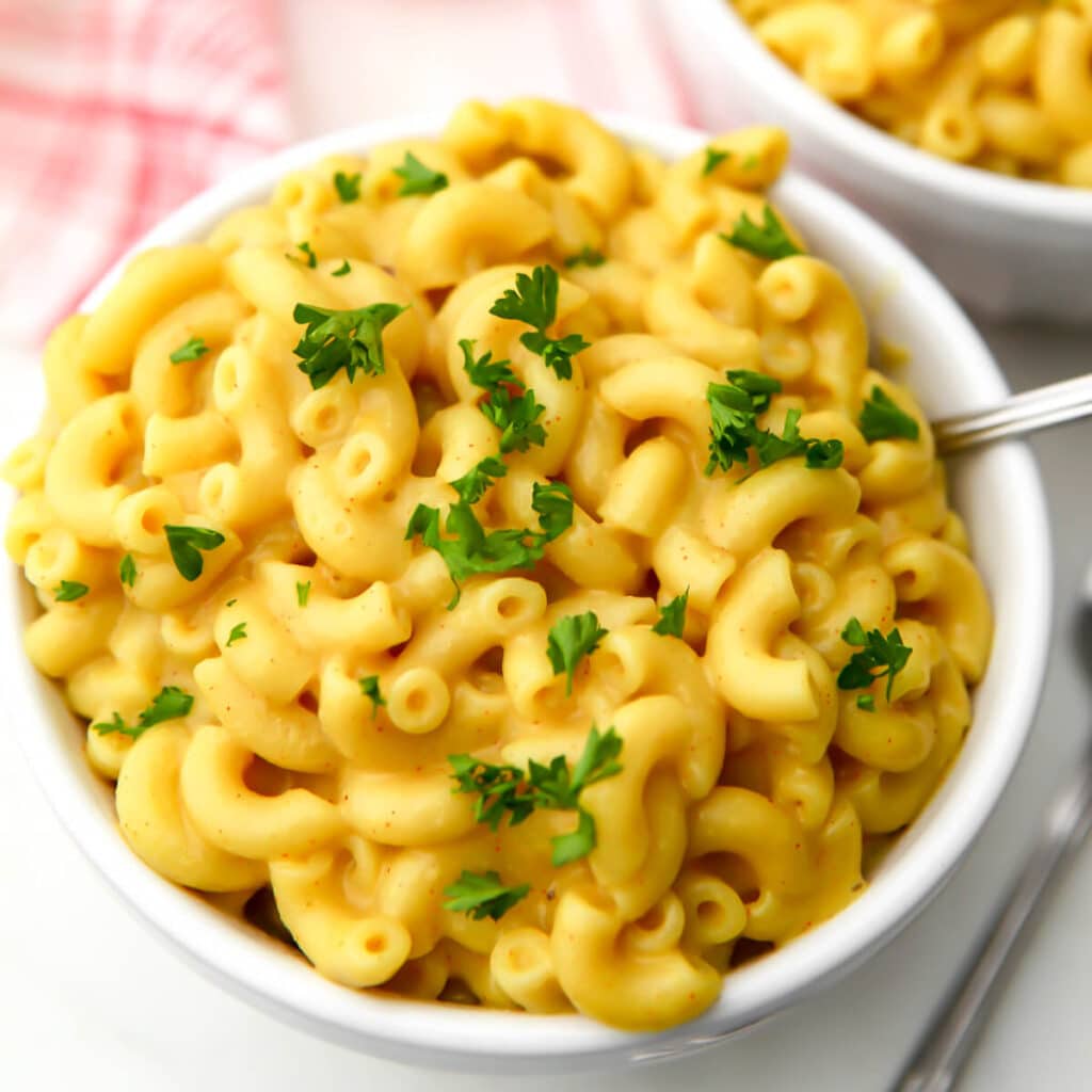 A top view of a bowl of coconut milk mac and cheese with parsley sprinkled on top and a fork in the bowl.