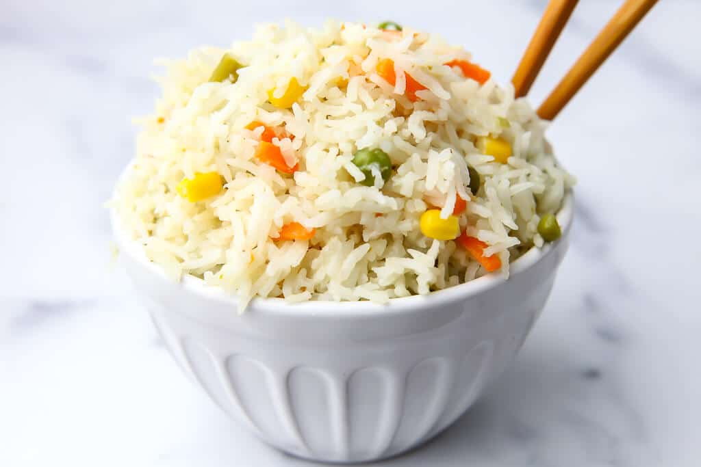 A white bowl filled with Thai coconut rice with chop sticks in it.