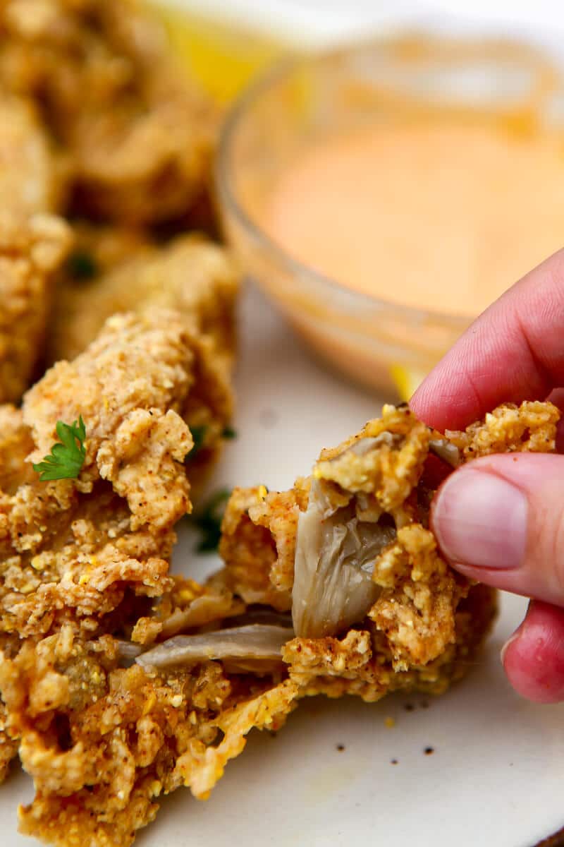 A piece of a vegan deep fried oyster mushroom ripped open to see the inside.