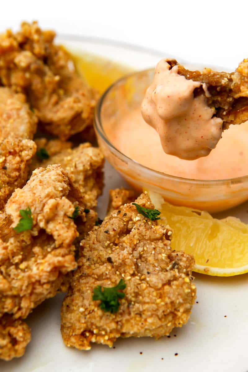 Fried oyster mushrooms on a white plate with one being dipped into chipotle mayo.