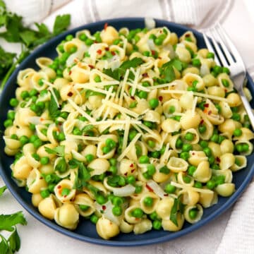 A blue plate filled with green pea pasta made with small pasta shells and garnished with parsley.