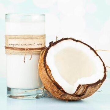 A glass of coconut milk next to an open coconut.