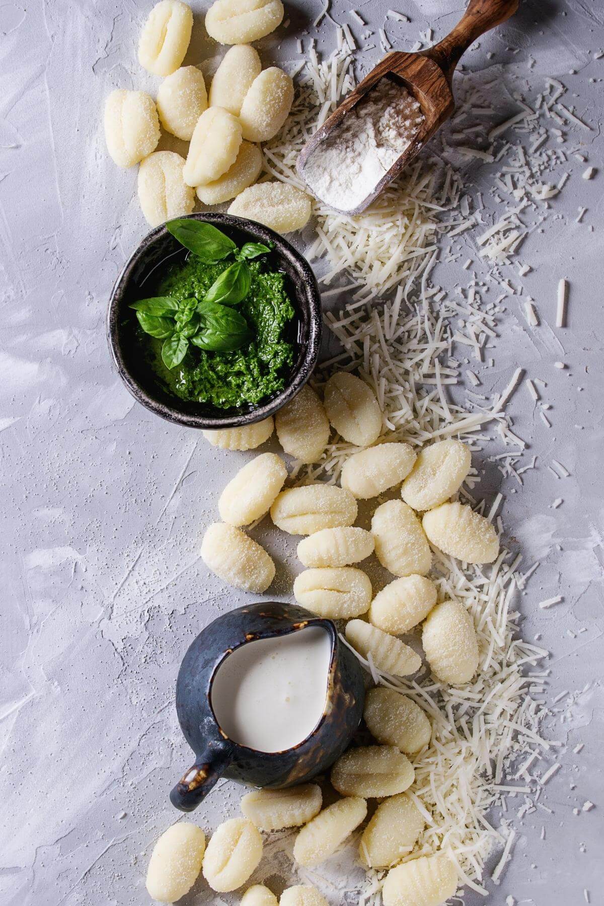 Gnocchi scatter around on a light blue background with basil, milk, and cheese.