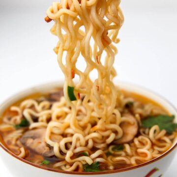 A bowl of ramen noodle soup with the noodle being lifted out with chopsticks.