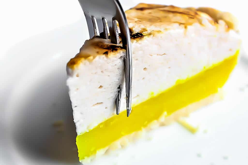 A slice of a lemon meringue pie with a fork in it.
