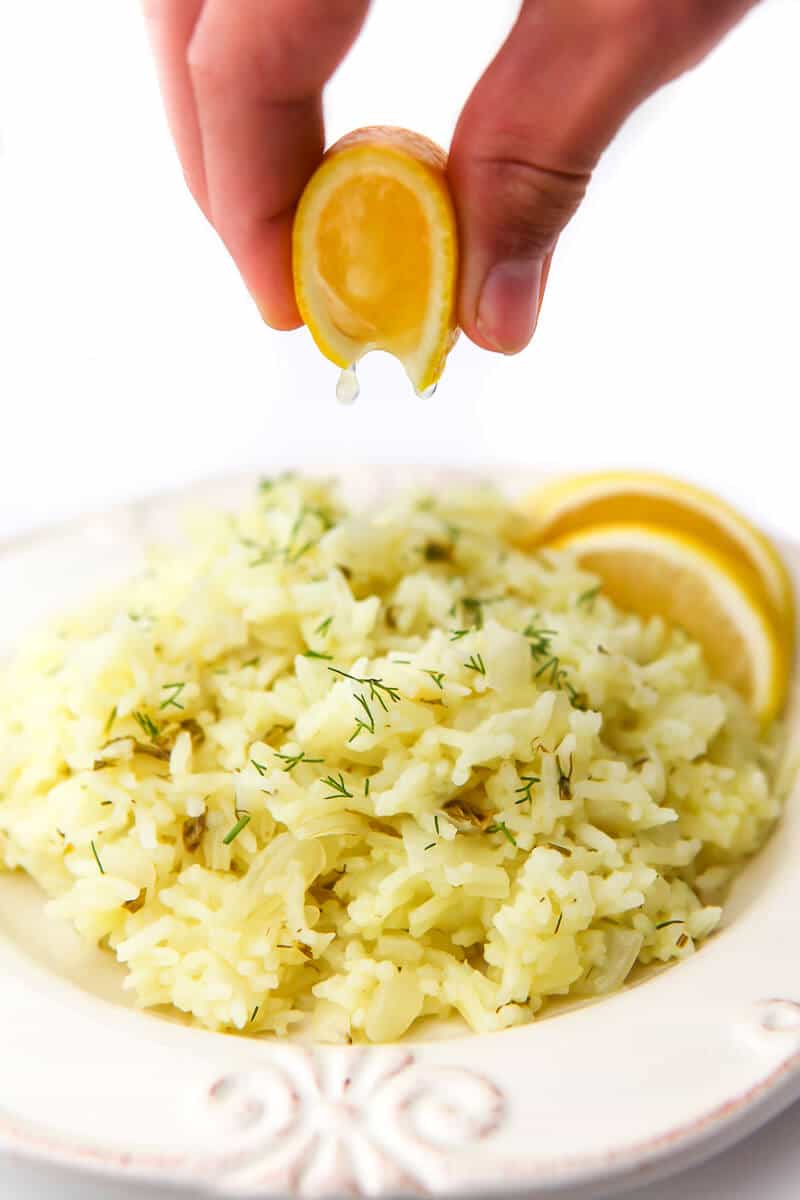 Someone squeezing a lemon slice over top of a white plate full of lemon rice.