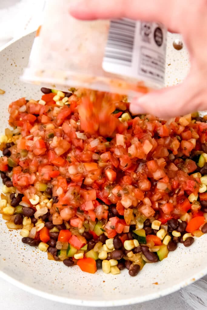 A container of salsa being added to a vegan Mexican stir-fry.