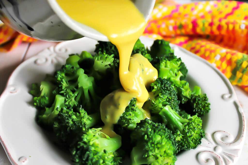 Vegan nacho cheese sauce being poured over steamed broccoli.