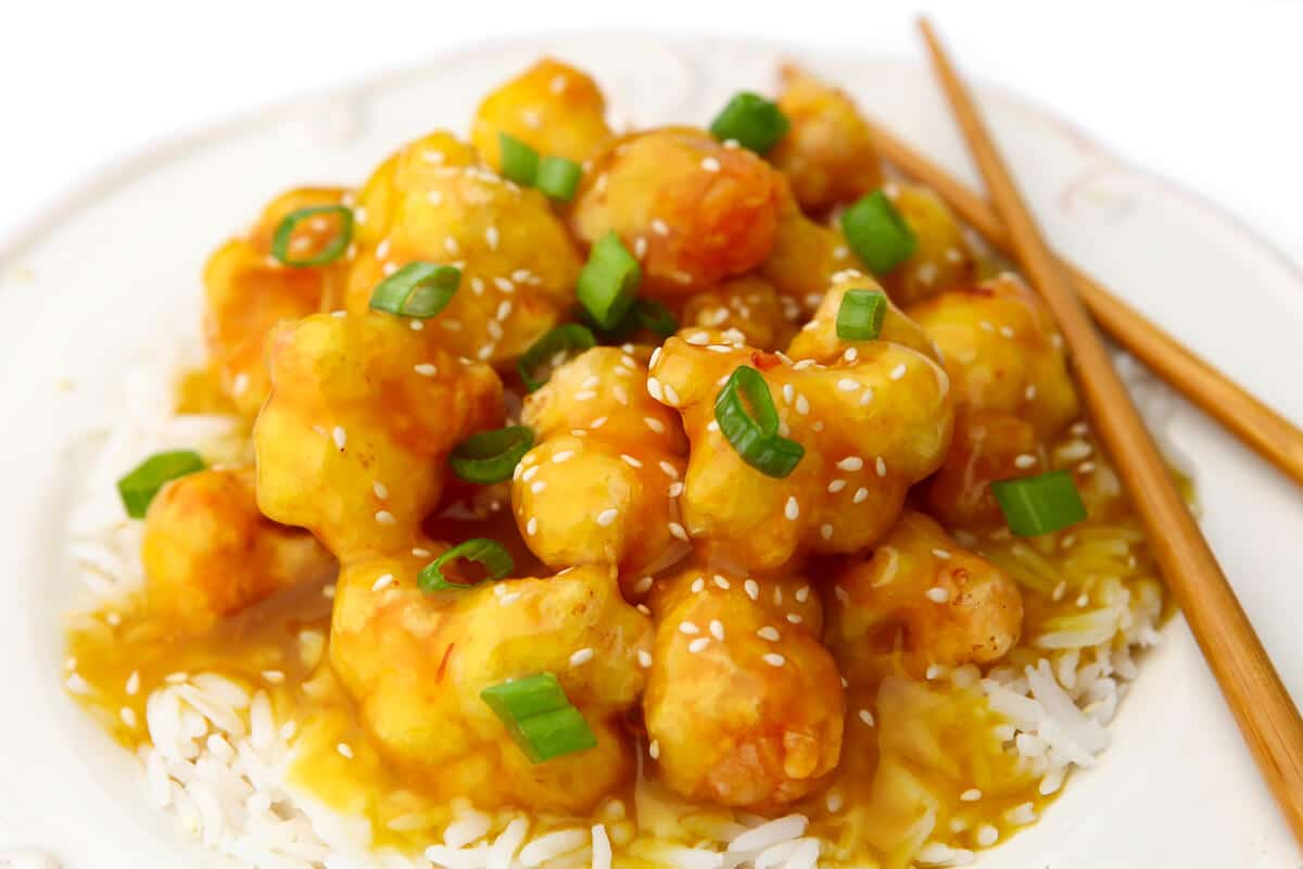 A white plate with white rice and vegan orange cauliflower with chopsticks on the side.