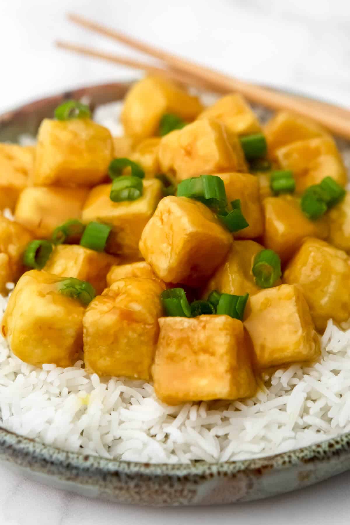 Vegan orange tofu on a bed of white rice sprinkled with green onions.