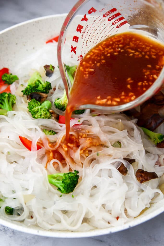 Pouring the stir fry sauce over the vegetables and glass noodles to make pad woon sen.