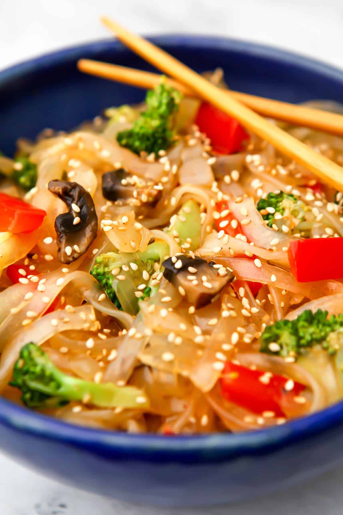 Pad woon sen noodles with vegetables in a blue bowl sprinkled with sesame seeds.