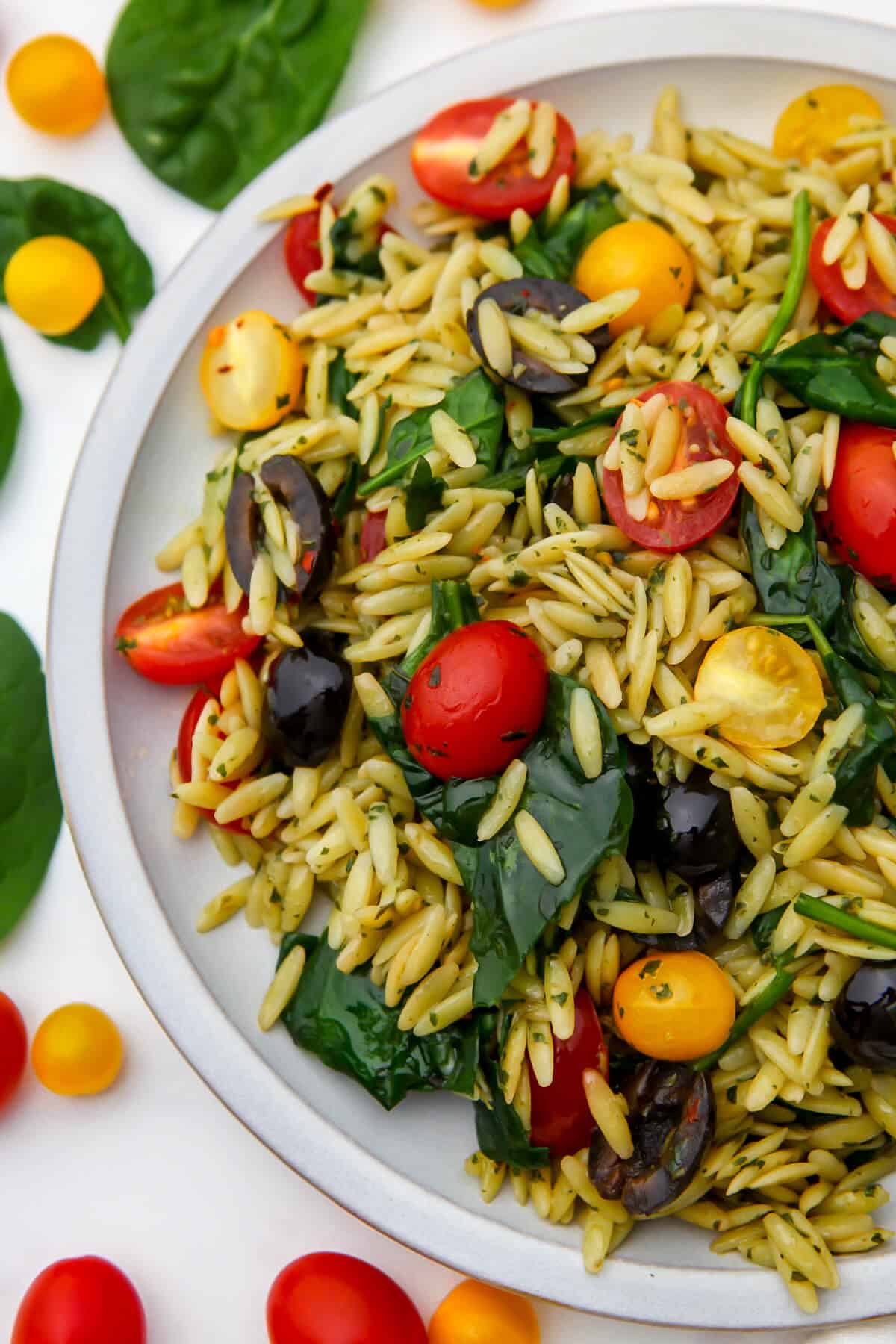 A pesto orzo pasta salad with tomatoes and spinach on a white plate with colorful cherry tomatoes on the side.