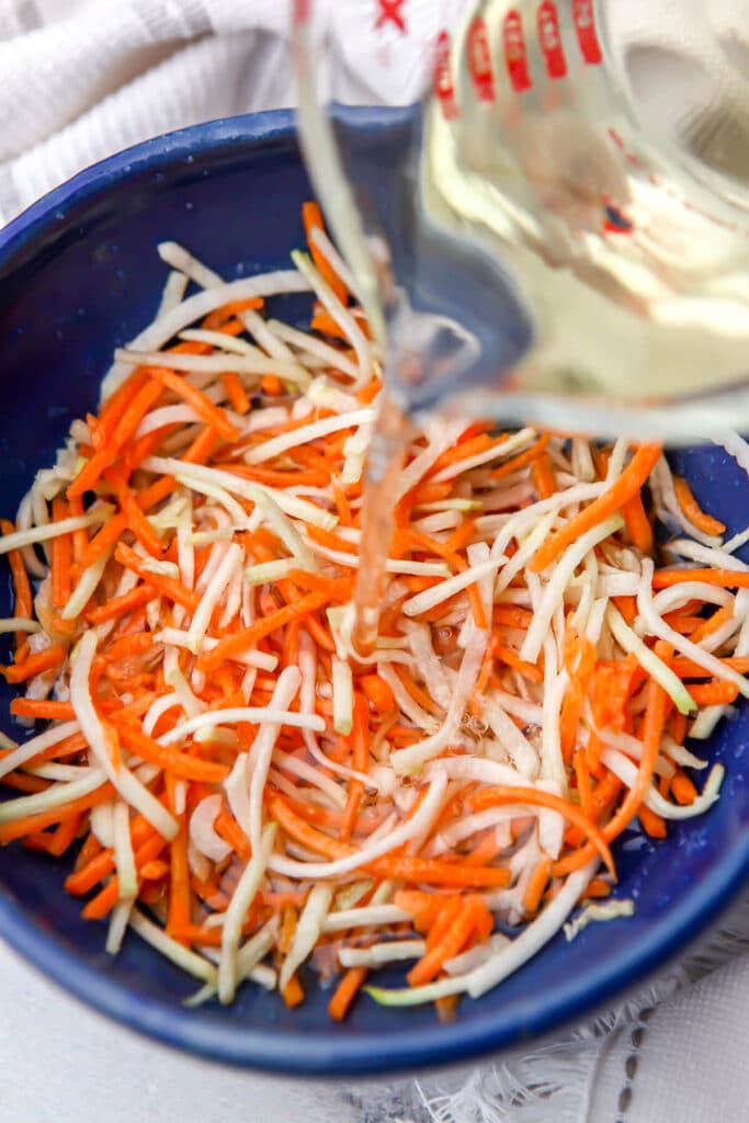 Pouring vinegar over carrots and daikon after they have been sprinkled with sugar and salt.