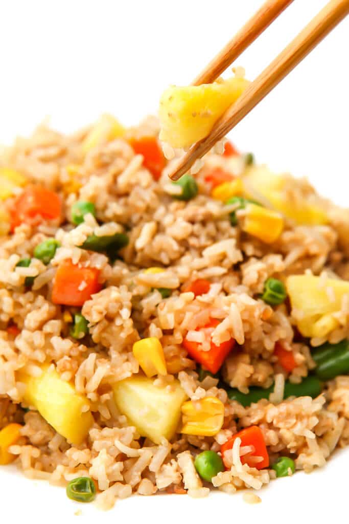 A white plate filled with pineapple fried rice with chop sticks picking up a piece of pineapple. 