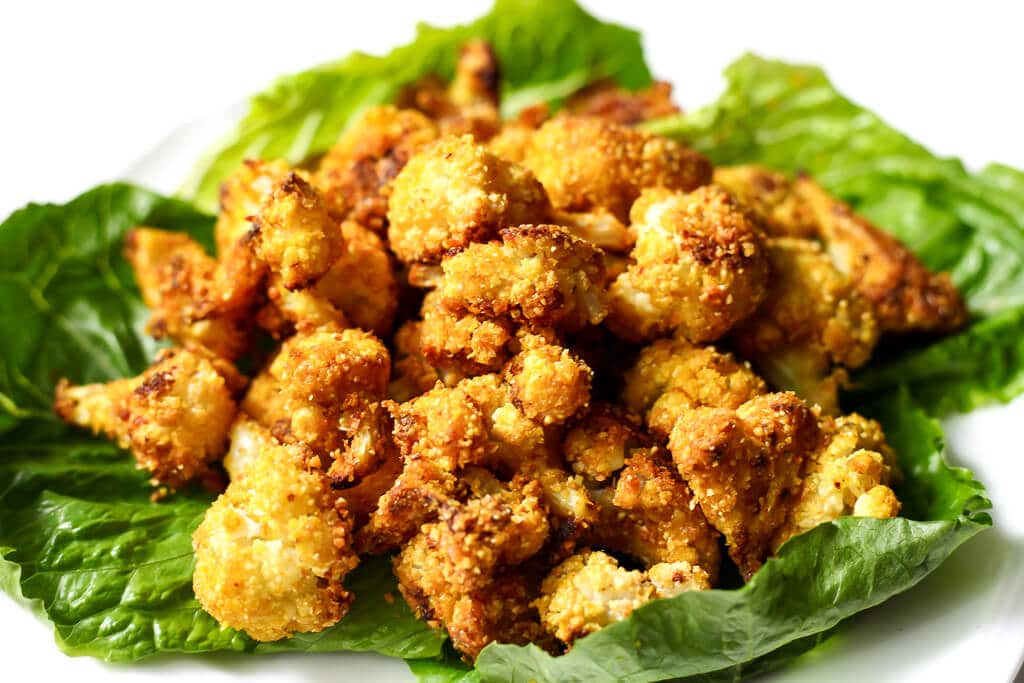 A white plate with a bed of lettuce and roasted cauliflower nuggets.