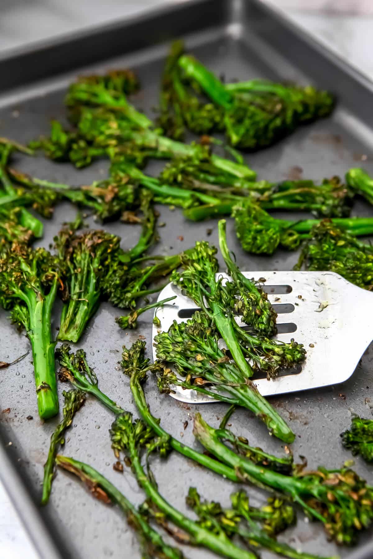 Roasted tender stem broccoli on a baking sheet being flipped with a spatula.