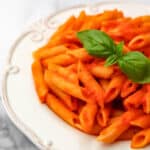 Vegan roasted tomato and pepper sauce over pene pasta with a basil leaf on top.