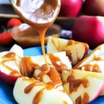 A blue plate with sliced apples with vegan salted caramel sauce being poured over the apples.