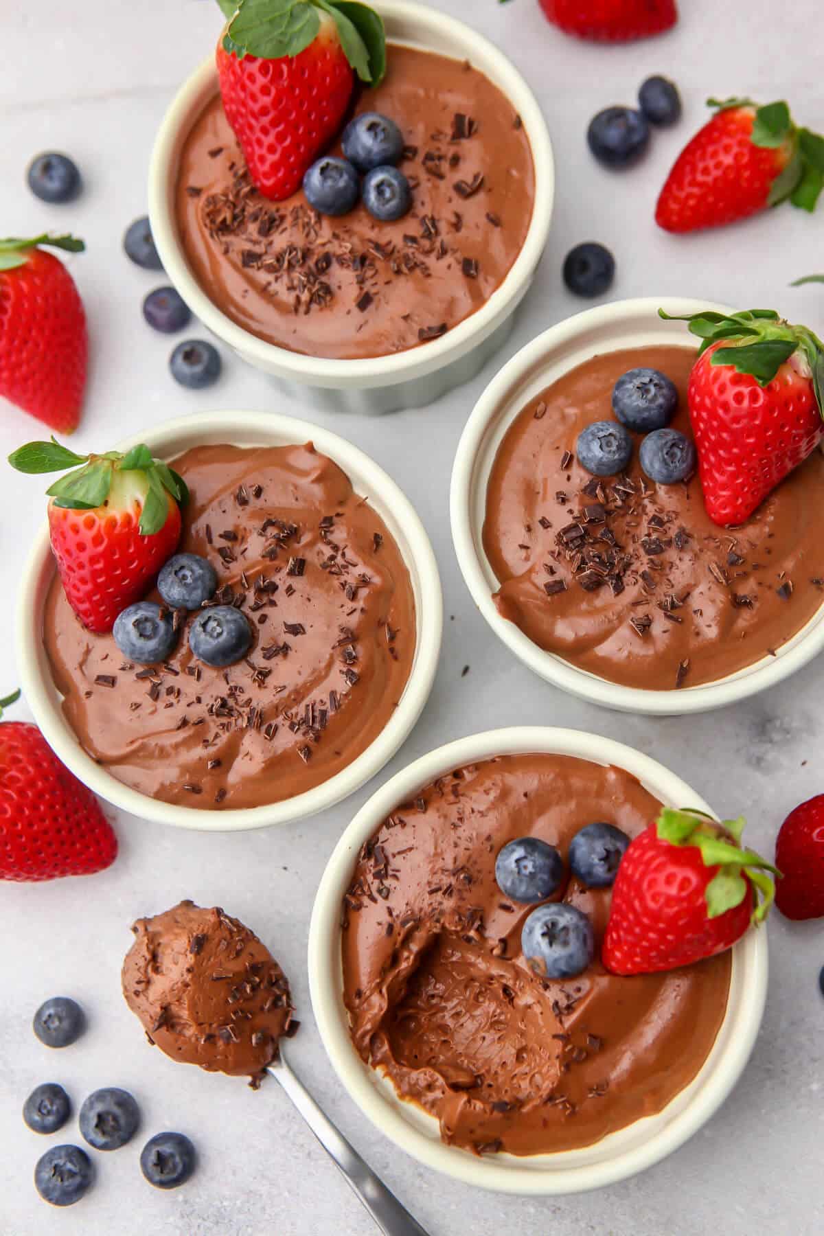 A top view of tofu chocolate mousse with berries on top with a spoonful taken out of one cup.