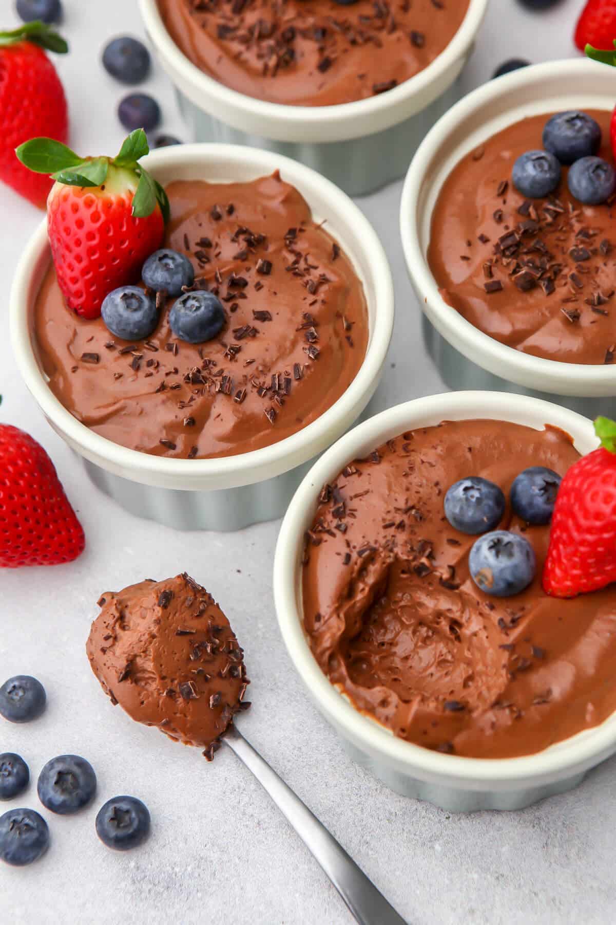 Vegan chocolate mouse cups with berries on top with a scoop taken out of one of them.