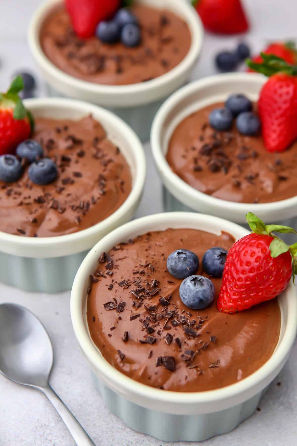 Four cups of vegan chocolate mousse with berries and chocolate shavings on top.