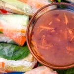 Sweet chili sauce in a glass bowl next to spring rolls.