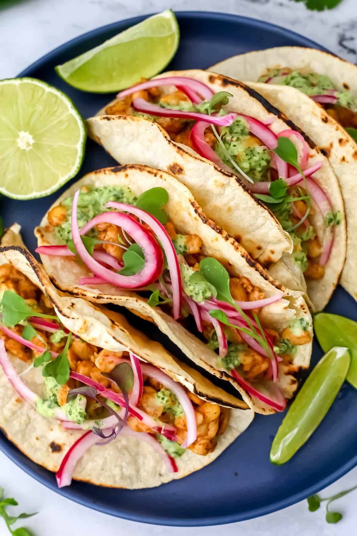 A top view of 4 soft shell tempeh tacos with cilantro lime sauce and pickled onions in them.