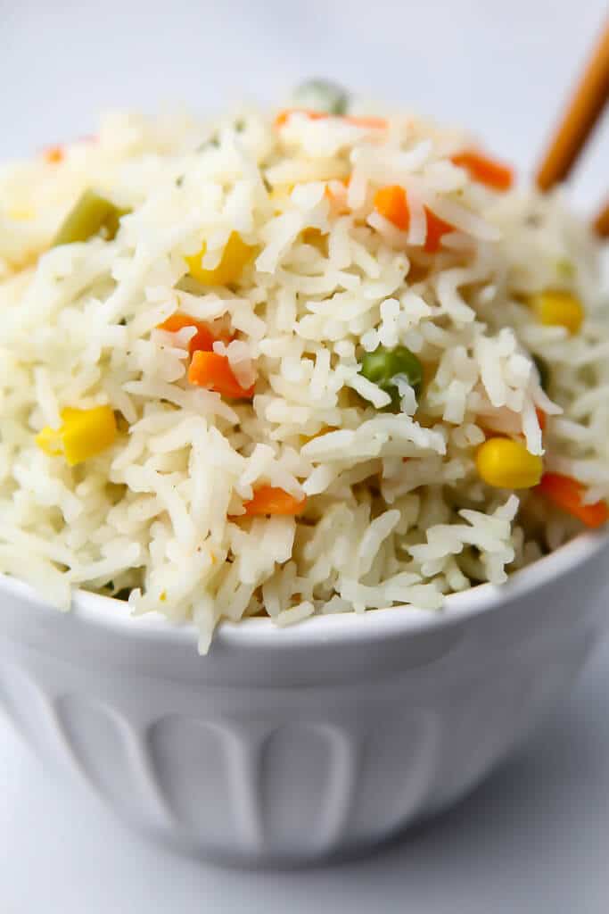 Curry coconut rice with vegetables in a white bowl.