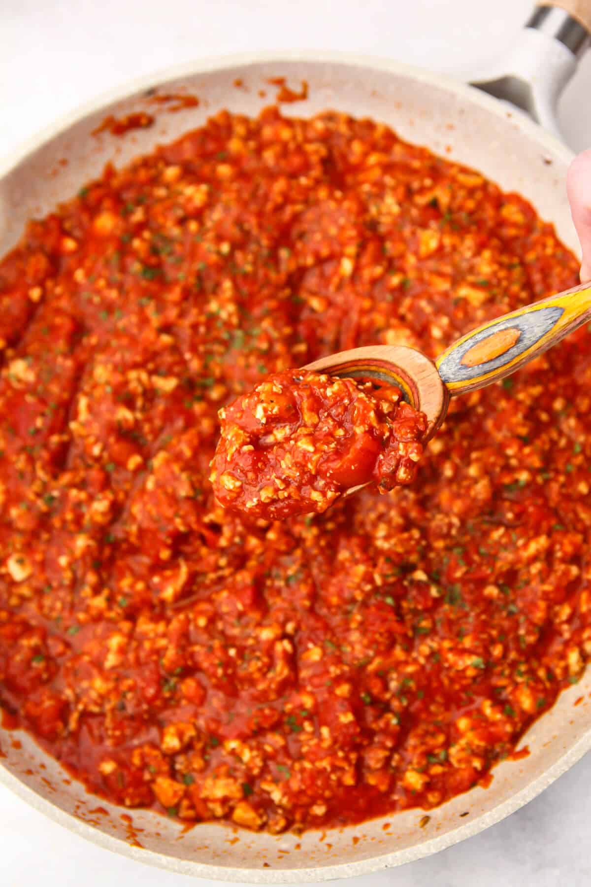 A frying pan filled with tofu pasta sauce with a wooden spoon scooping up some sauce.