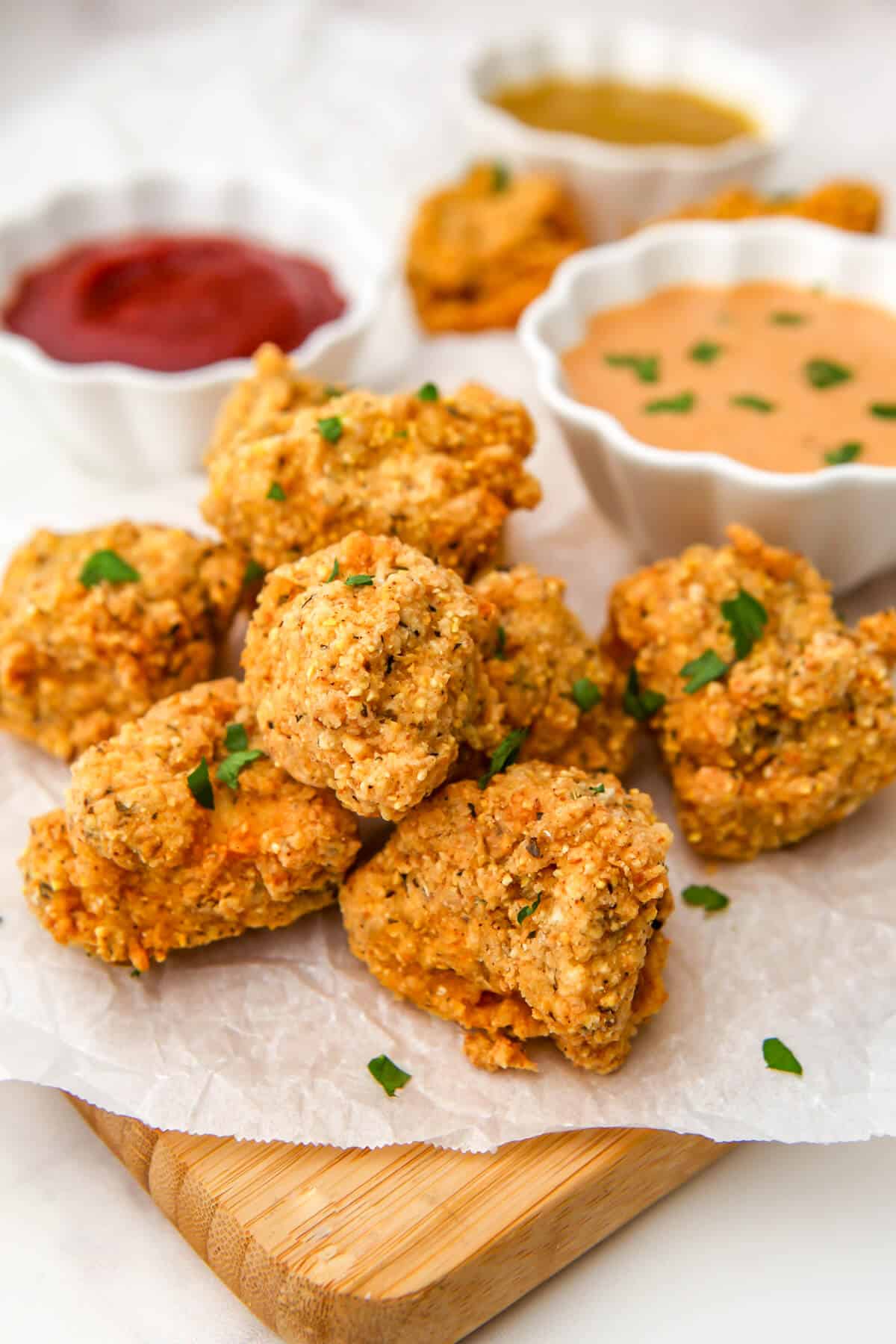 A cutting board topped with deep fried tofu nuggets served with 3 dipping sauces.