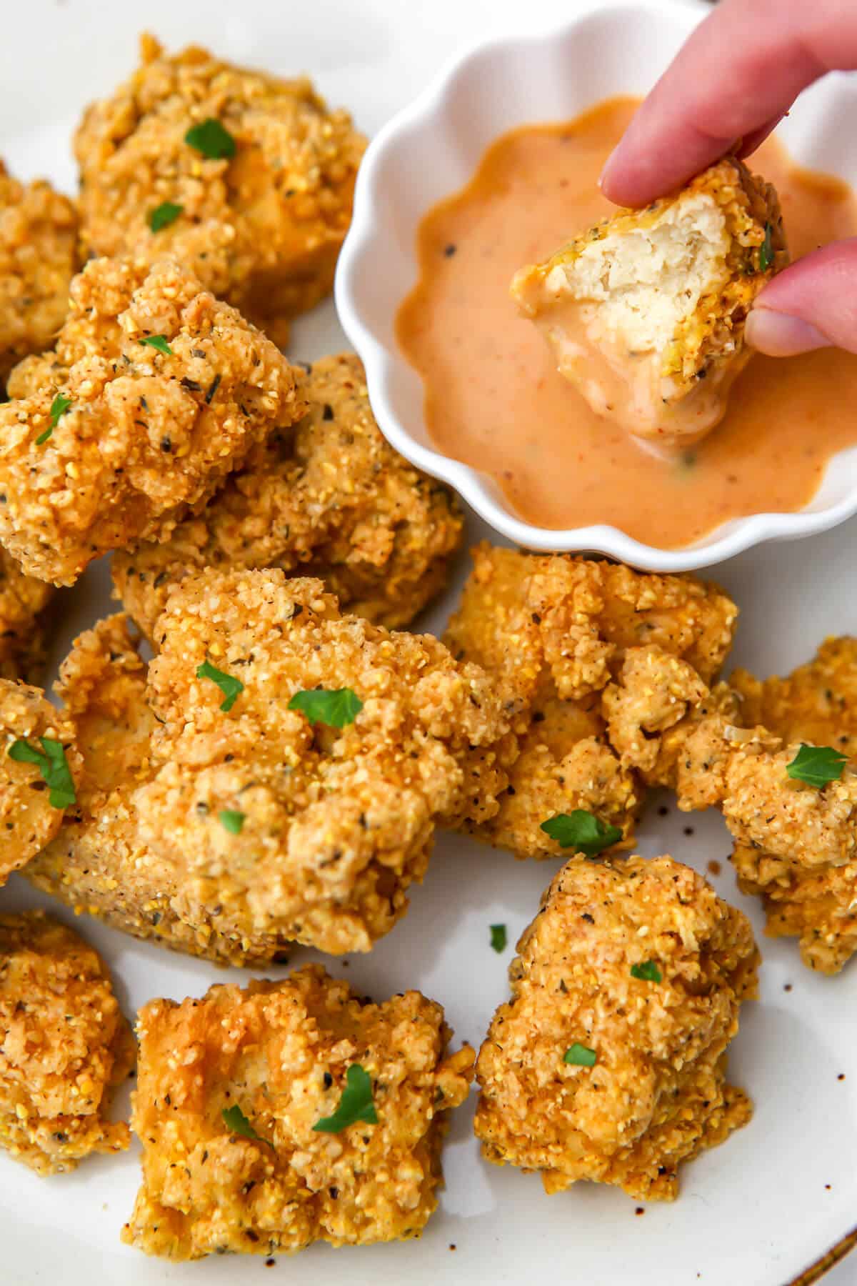 Vegan tofu fried chicken on a white plate with a piece bein dipped into sauce.