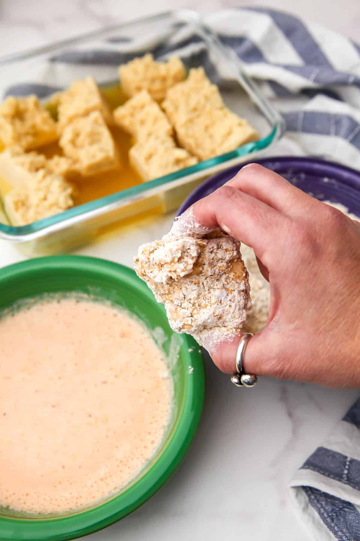 Someone holding a chunk of tofu that has been marinated and breaded before frying.