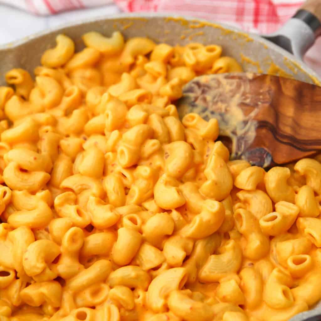 A pan full of vegan tofu mac and cheese being stirred with a wooden spoon.