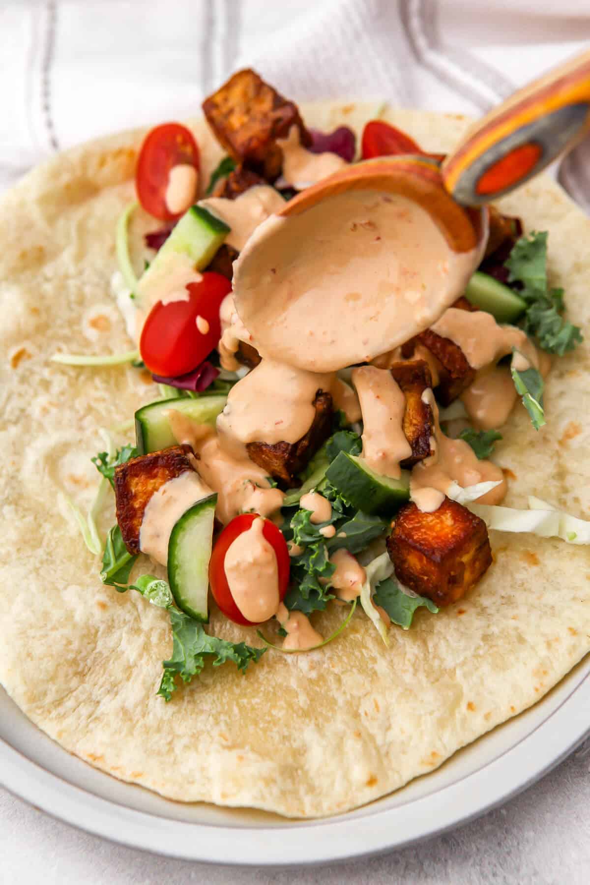 Spicy tahini sauce drizzled over tofu and veggies to make a tofu wrap.