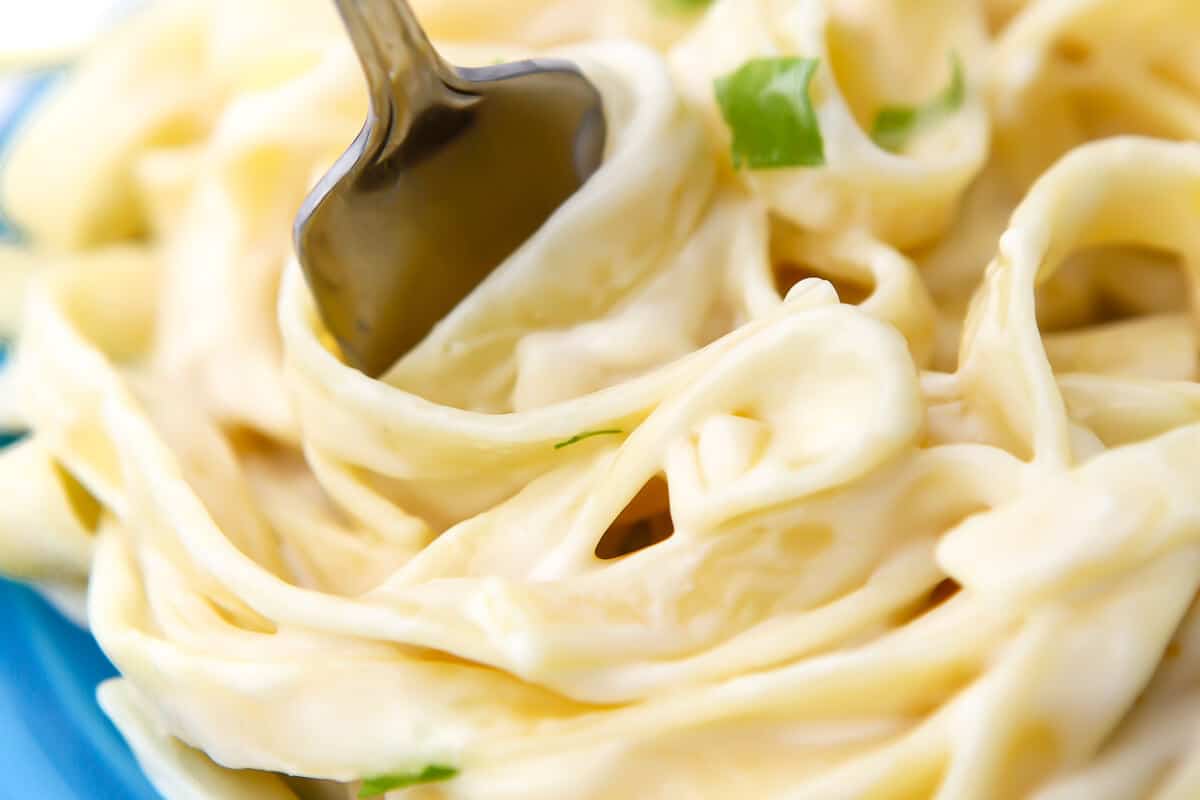 A close up of noodles with vegan Alfredo sauce on them being swirled with a fork.