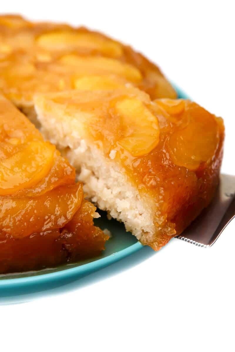 A vegan apple cake on a blue plate with a slice being taken out of it.