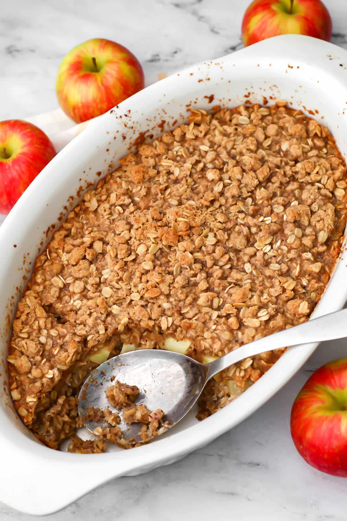 A white baking dish filled with vegan baked oatmeal with a crumb topping and apples around it.