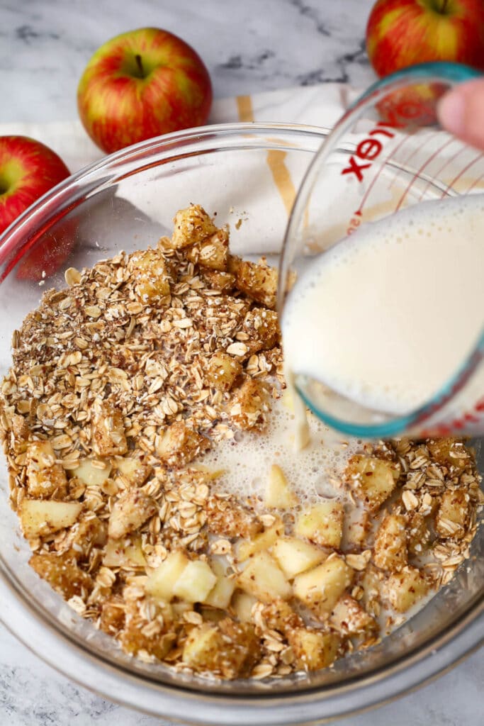 Vegan milk being added to dry ingredients and apples to make baked oatmeal.