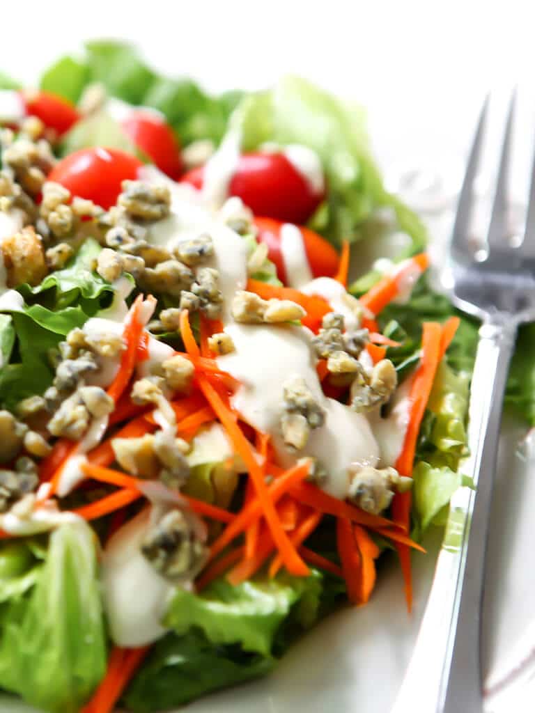 A salad with vegan blue cheese dressing and vegan blue cheese crumbles on top and a fork on the side.