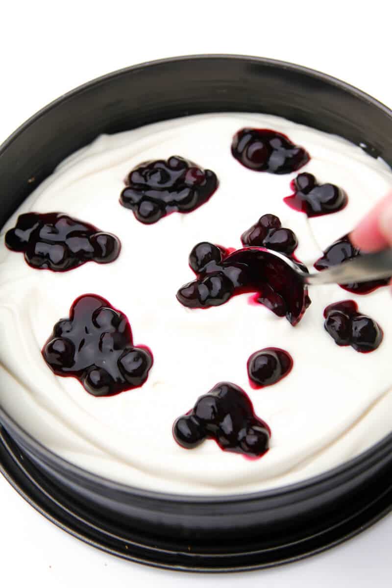 A no-bake vegan cheesecake with blueberry sauce dolloped on top of it before it's swirled in.