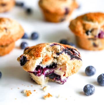 Vegan blueberry muffins on a white background with fresh blueberries around them.