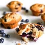 Vegan blueberry muffins on a white background with fresh blueberries around them.